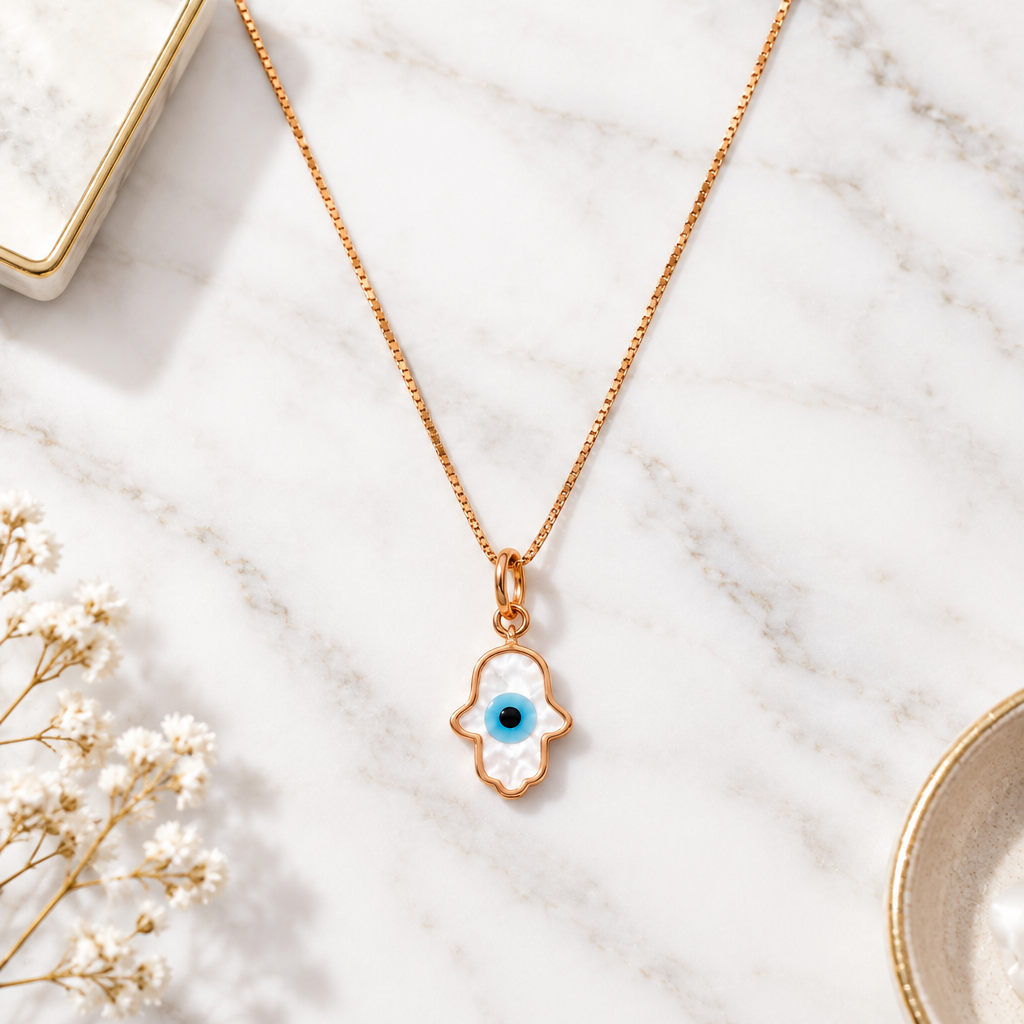 Gold hamsa hand pendant outlined in white enamel with a blue evil eye center. Protective gifts for her under Ra, 15,000