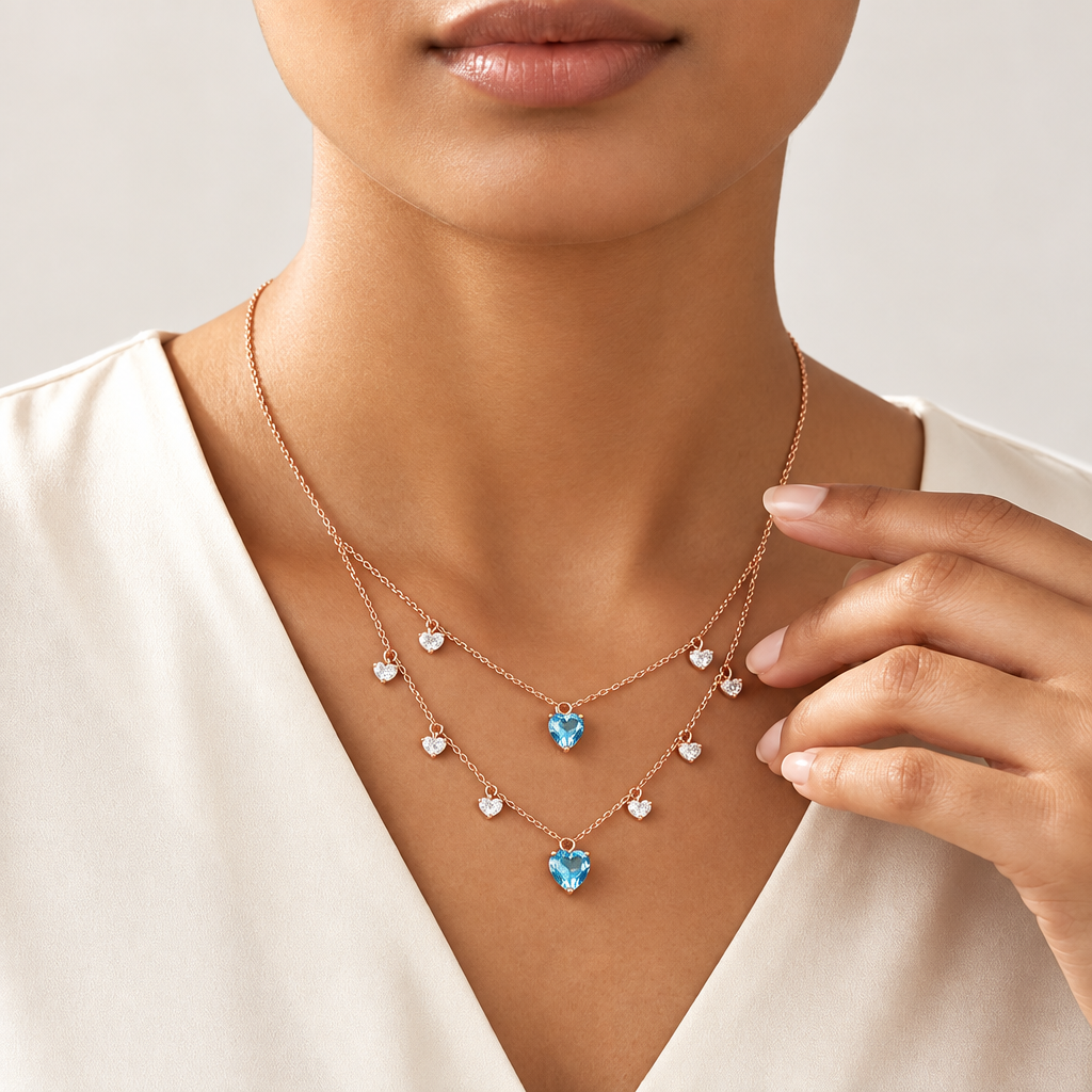 Layered rose gold necklace with clear crystal diamond drops and two blue heart-shaped gemstone pendants priced under Rs. 2,00,000