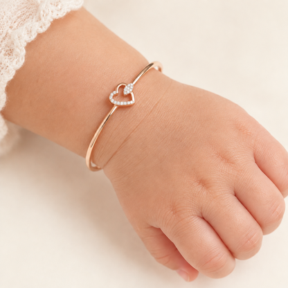 Rose gold bangle-style bracelet with an open diamond heart charm.