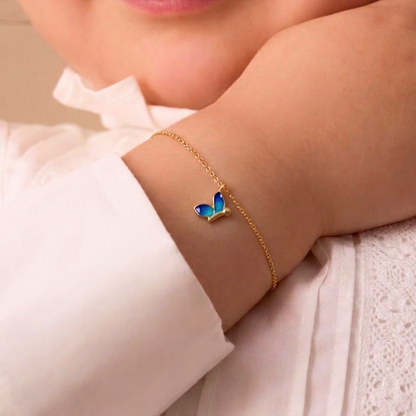 Gold chain bracelet with an enamel blue butterfly charm dangling, worn on a baby's wrist priced under Rs. 30,000.