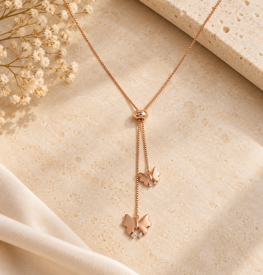 Rose gold lariat necklace with two dangling butterfly charms below a small oval clasp.