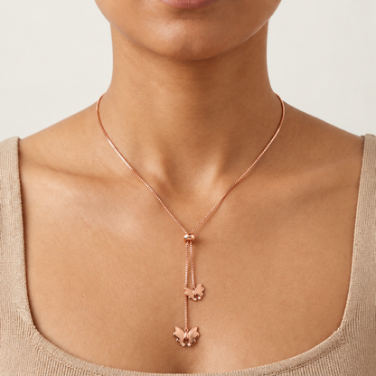 Rose gold lariat necklace with two dangling butterfly charms below a small oval clasp.