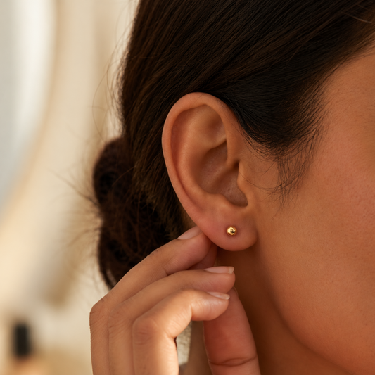 Pair of polished 18kt gold ball stud earrings on a soft neutral surface. Perfect for second piercings, Kids under Rs. 15,000
