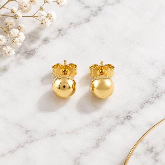Pair of polished 18kt gold ball stud earrings on a soft neutral surface. Perfect for second piercings, Kids under Rs. 15,000