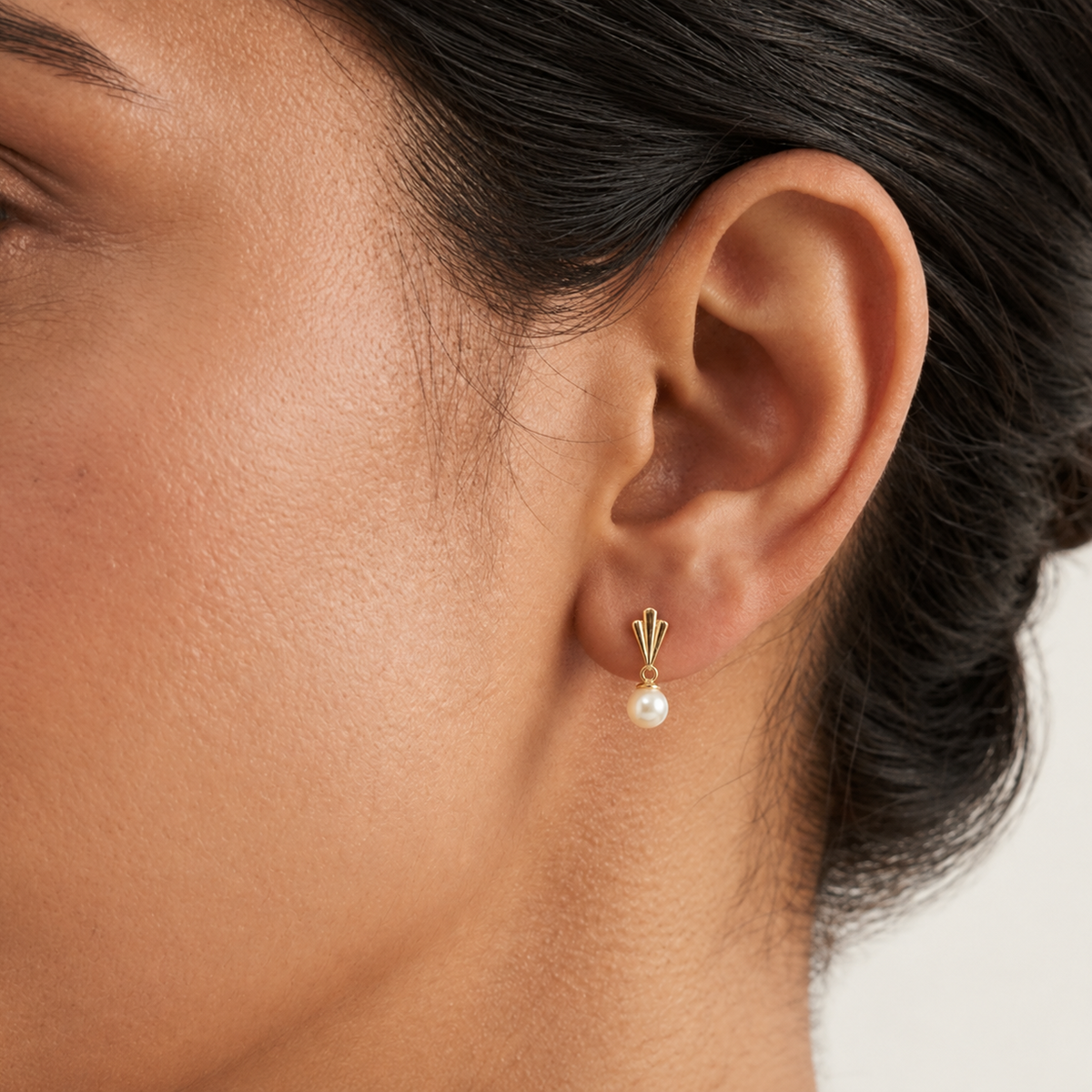 Gold drop earrings with a fluted cap and cream pearl worn on ear. A perfect gift for her under Rs. 40,000