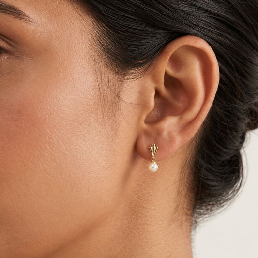 Gold drop earrings with a fluted cap and cream pearl worn on ear. A perfect gift for her under Rs. 40,000