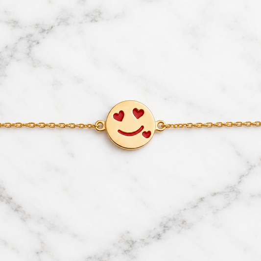 Gold bracelet with a round disc charm featuring a smiley face and red heart eyes. Cute gold gifts for kids under Rs. 40,000