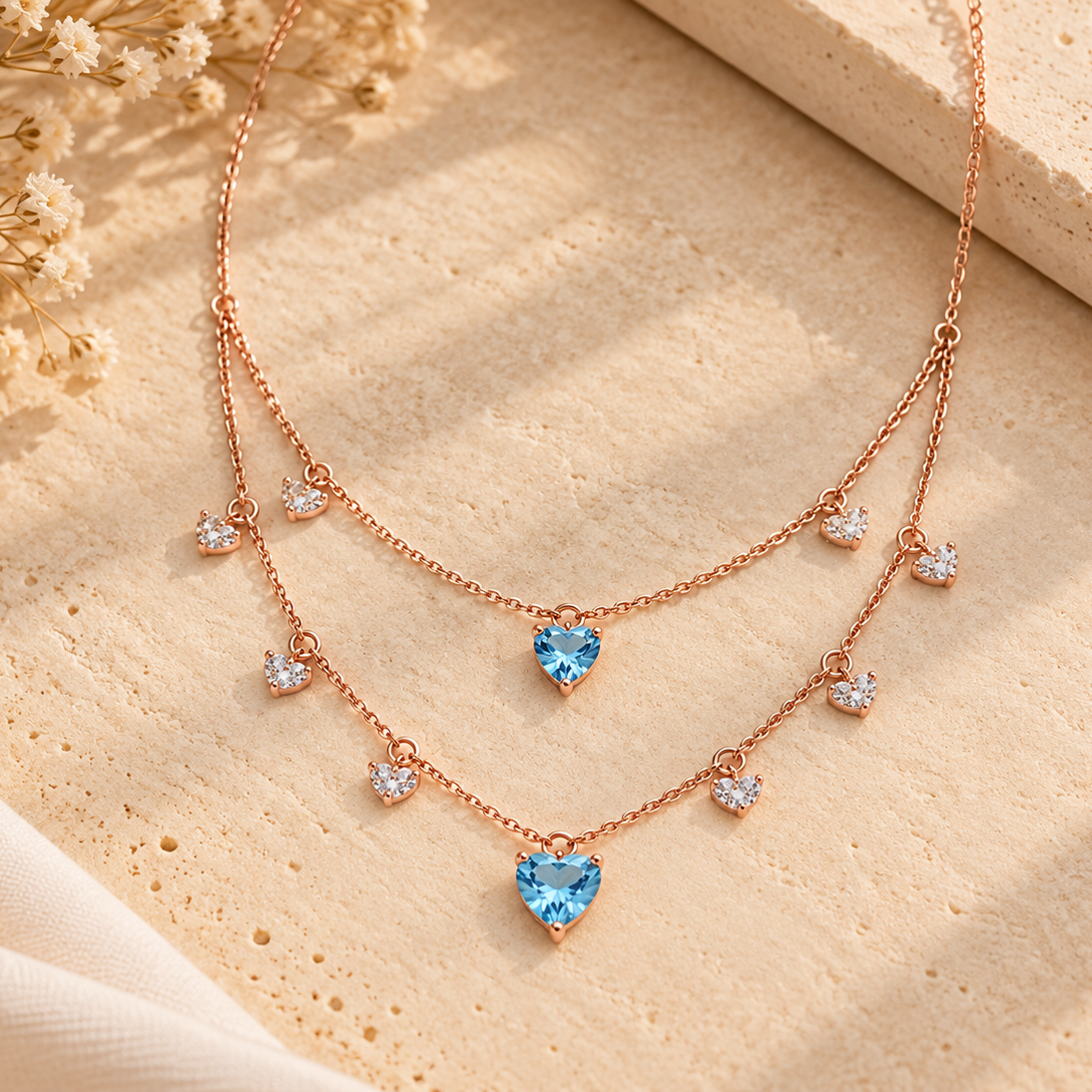 Layered rose gold necklace with clear crystal diamond drops and two blue heart-shaped gemstone pendants priced under Rs. 2,00,000