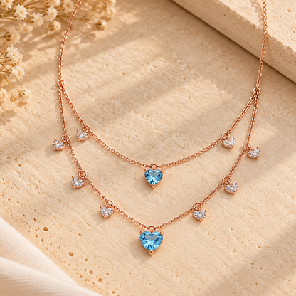 Layered rose gold necklace with clear crystal diamond drops and two blue heart-shaped gemstone pendants priced under Rs. 2,00,000