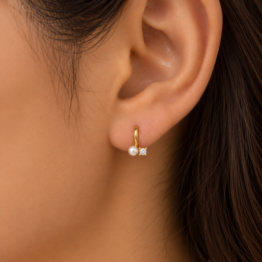 Gold huggie earrings with a white pearl drop and a diamond baguette accent, priced under Rs. 20,000