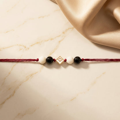 Geometric square gold Rakhi with black and white beads.