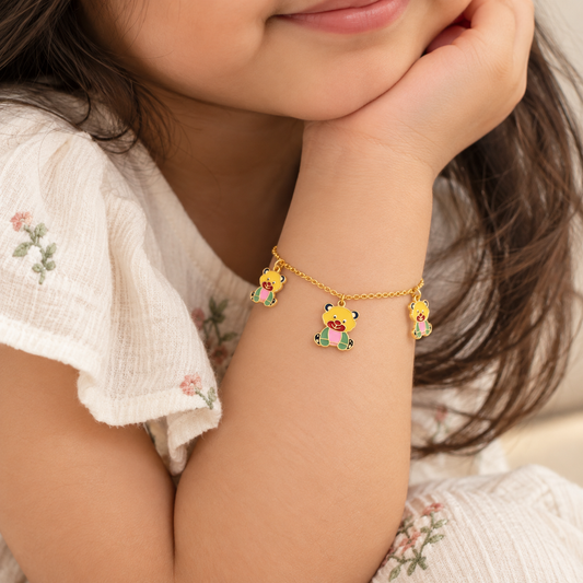 Gold chain bracelet with three colorful enamel teddy bear charms, worn on a baby's wrist.