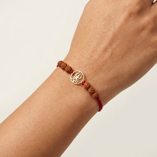 Gold Trishool Rakhi with Rudraksha beads on a wrist.